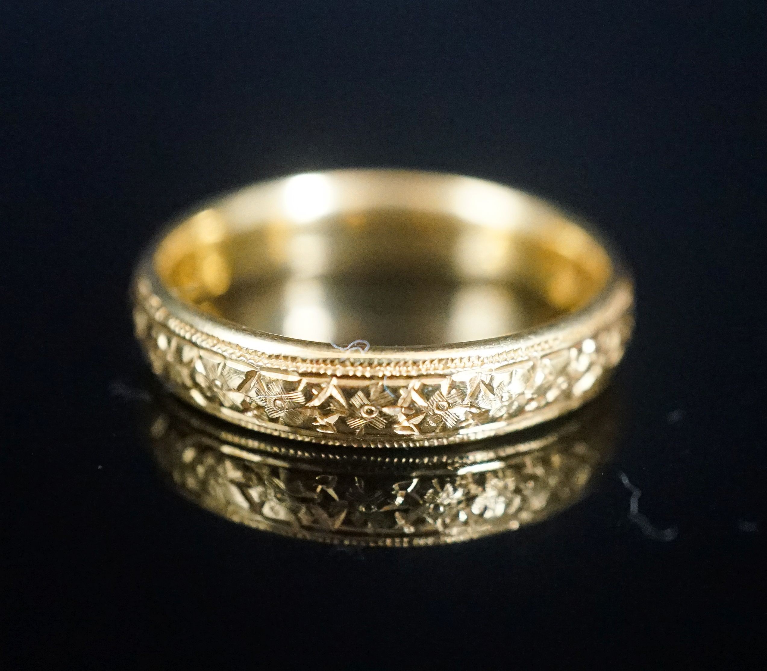 A George V bright cut engraved 22ct gold wedding band, decorate with flower heads, London, 1918, size V, 8 grams.